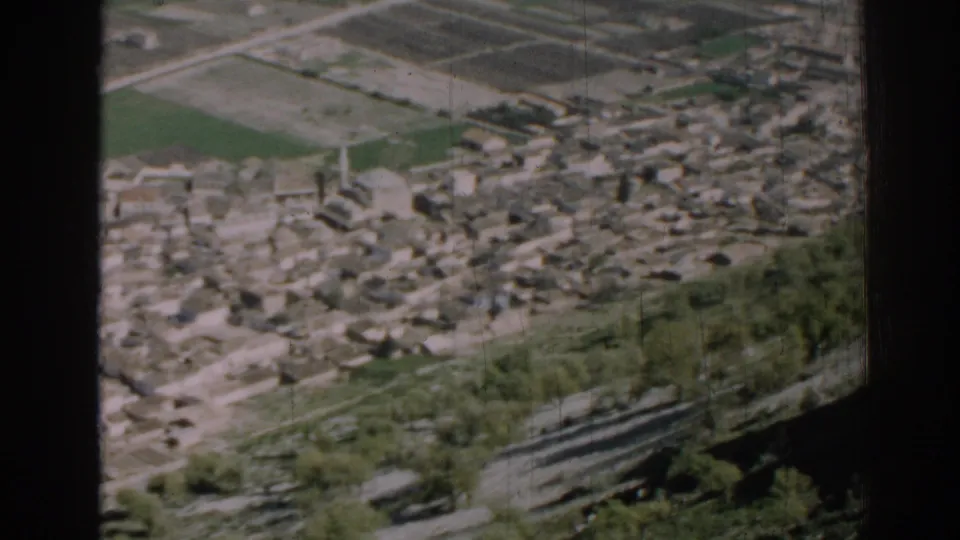 Late clip frame from 1962 Izmir showing buildings, agricultural plots, roads, hillside trees, and dark film or window edges.