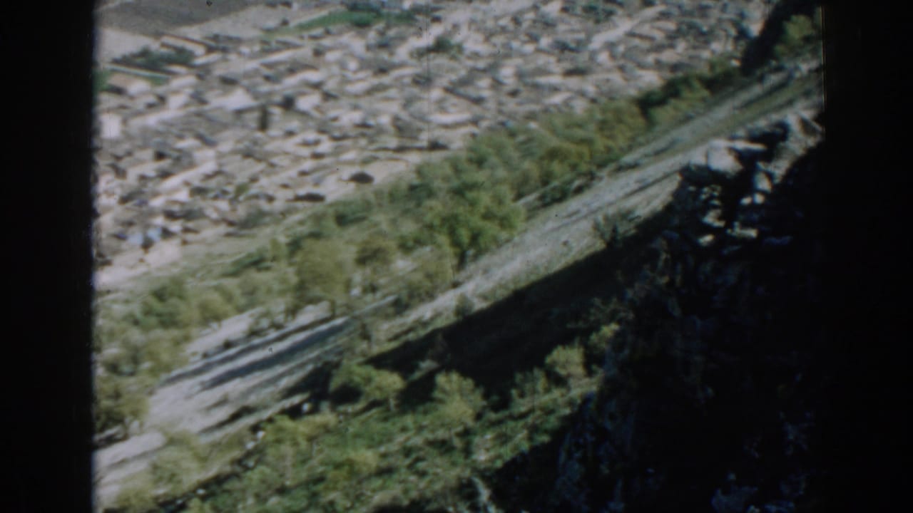 1962 Izmir home-movie frame showing a rocky slope with foliage and clustered buildings below.