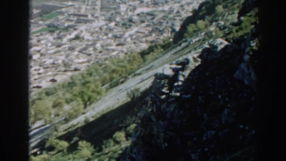 1962 8mm frame with soft motion blur, showing Izmir below a green rocky mountainside.