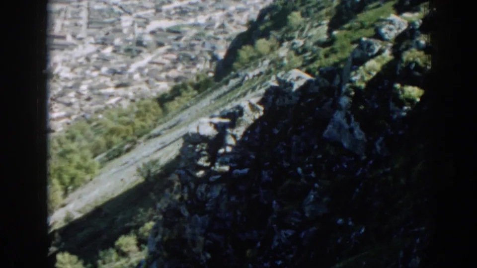 Izmir hillside view from 1962, with dark rocks, green vegetation, and city blocks below.