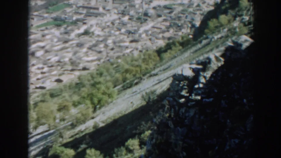 The camera frames dense Izmir rooftops above a steep, green and rocky hillside in soft 8mm focus.