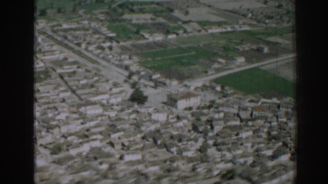 Aerial view of dense low-rise buildings, roads, and green fields beyond the neighborhood.