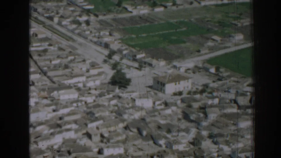 1962 Izmir aerial frame with a larger pale building, clustered rooftops, roadways, and surrounding green plots.