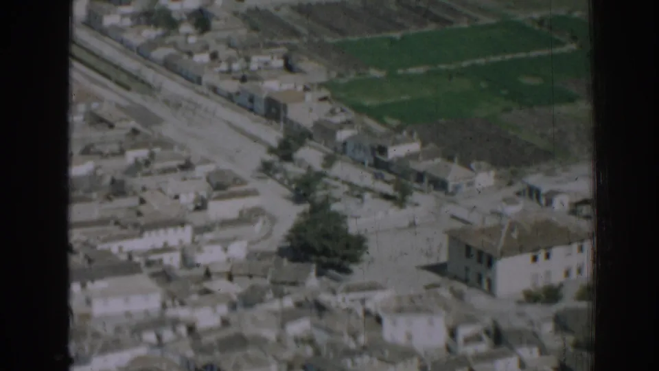 1962 Izmir, Turkey 8mm frame showing an aerial view of dense low-rise buildings beside a road, rail line, and fields.