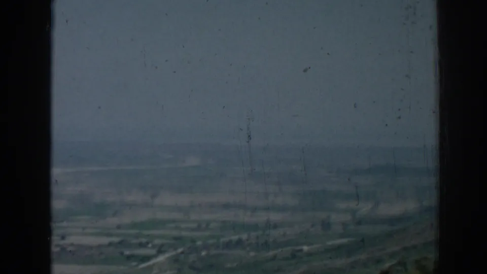 1962 Izmir, Turkey 8mm frame with a hazy aerial view over open terrain, fields, and distant built areas.
