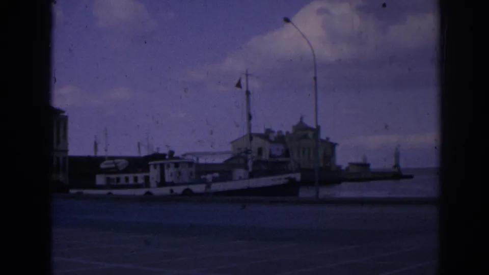 1962 Izmir, Turkey 8mm frame showing a waterfront with a moored vessel, street lamps, and harbor buildings.