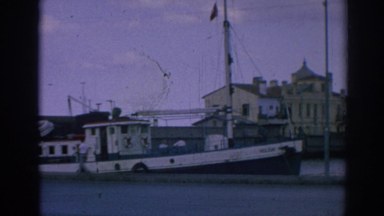 Tighter 1962 Izmir harbor frame showing the white docked boat near the quay, flag mast, lamppost, waterfront structure, and soft 8mm grain.