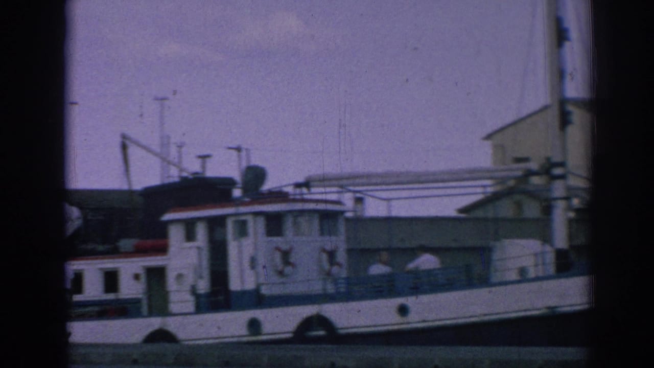 Side view of the white and blue tugboat HOLIDAY at a marina in Izmir, Turkey, with cabin details and dock structures visible.