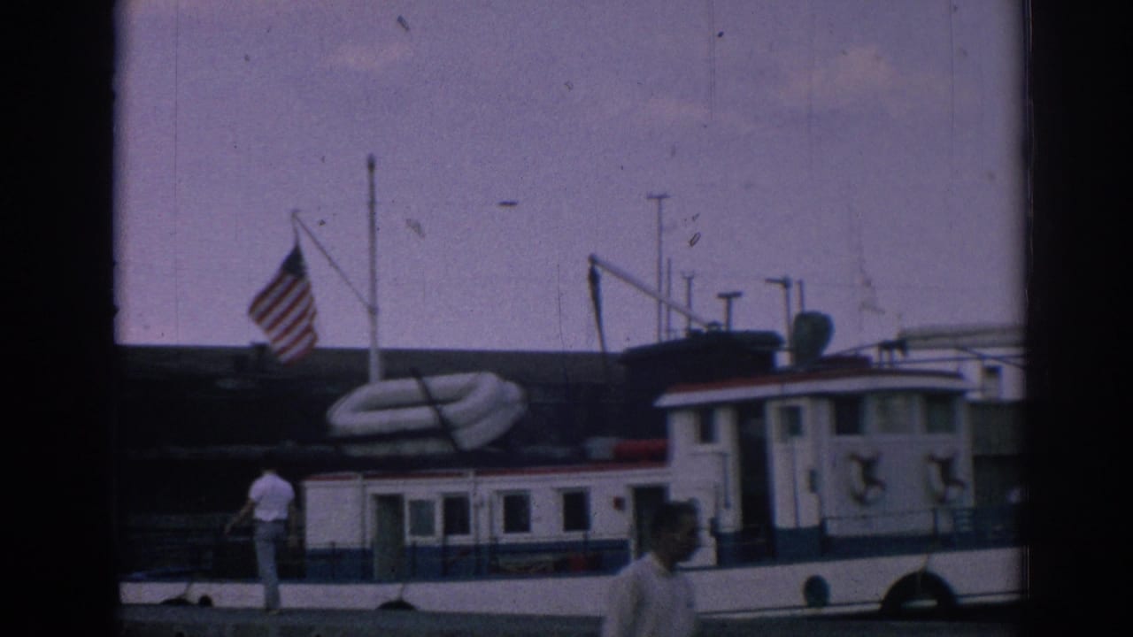 Final frame of the Izmir marina scene shows the docked tugboat, American flag, people on or near the pier, and a man passing in the foreground.