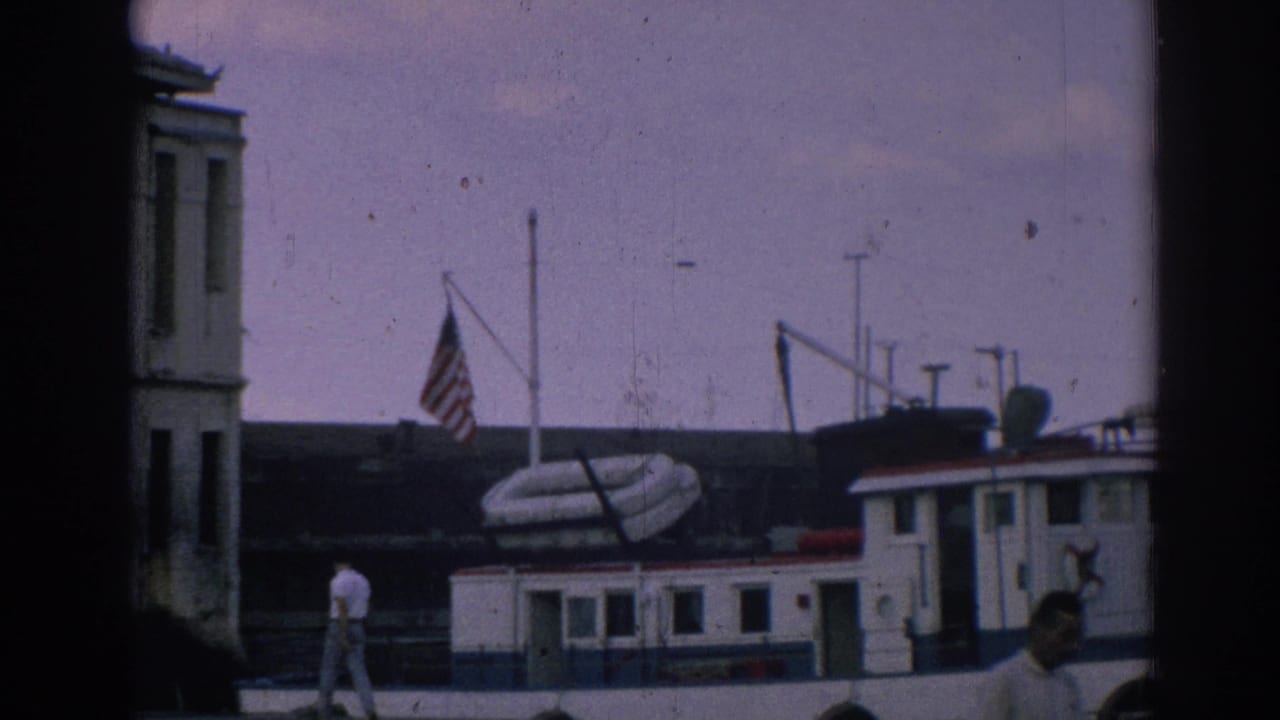 Docked boat with an American flag beside a waterfront building and a man walking on the dock.