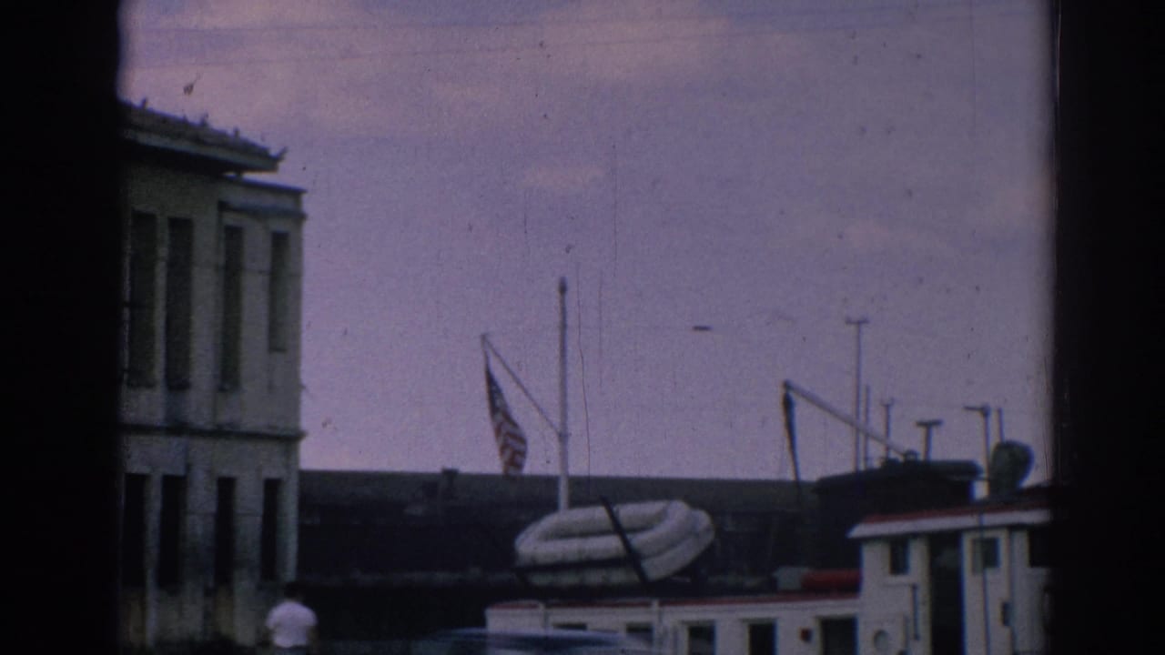 American flag fluttering over a small boat along the Izmir waterfront, with building facades and dock structures nearby.