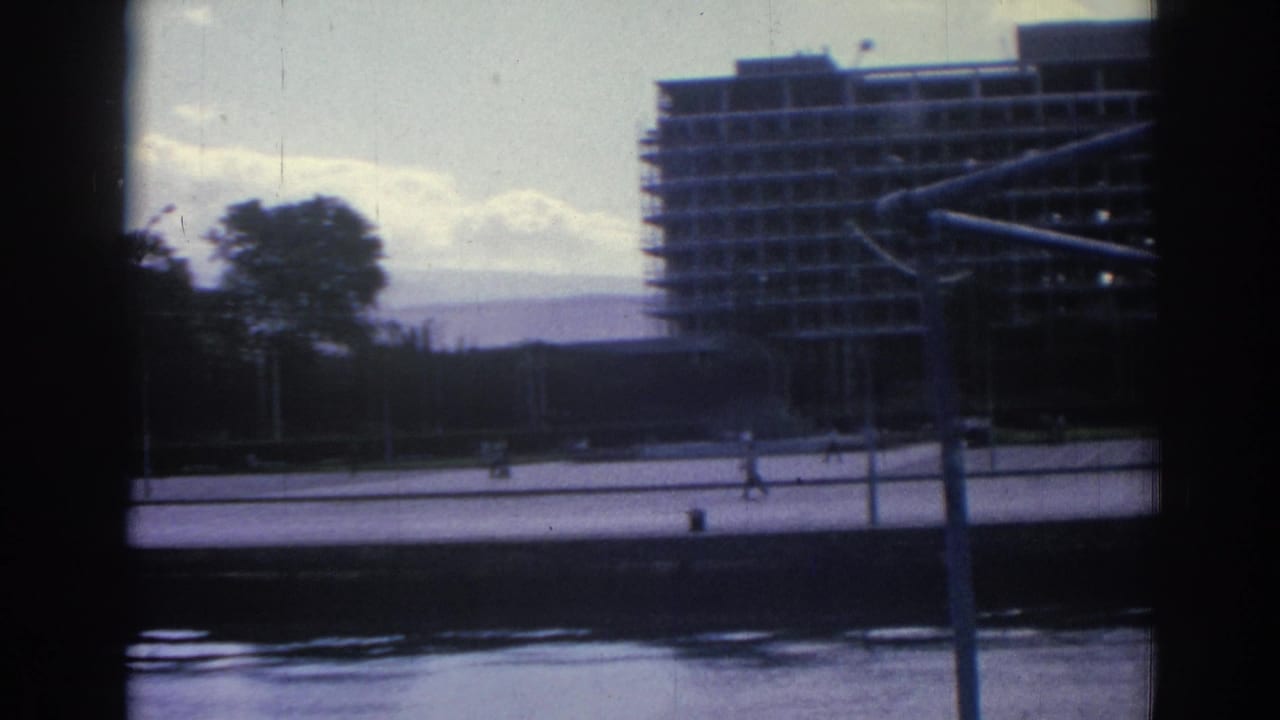 The camera looks from the boat across water toward an Izmir promenade, trees, and a large building under construction.