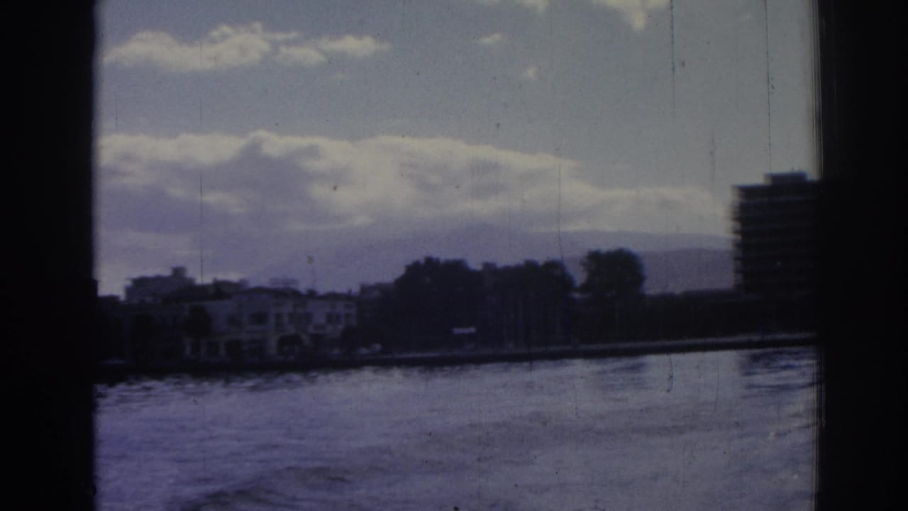 1962 Izmir waterfront view showing low buildings, tree line, distant hills, clouds, and a high-rise cropped at the right edge.
