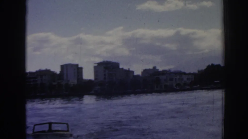 1962 Izmir home-movie frame showing a small motorboat near the bottom of the frame, rippled water, and an urban shoreline beyond.