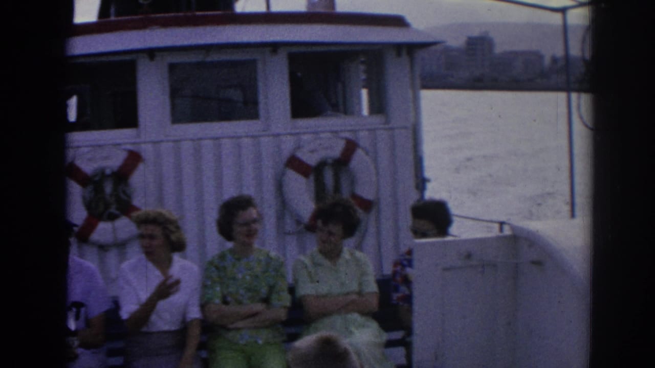 Adults seated on a ferry deck beside life rings and a white cabin.