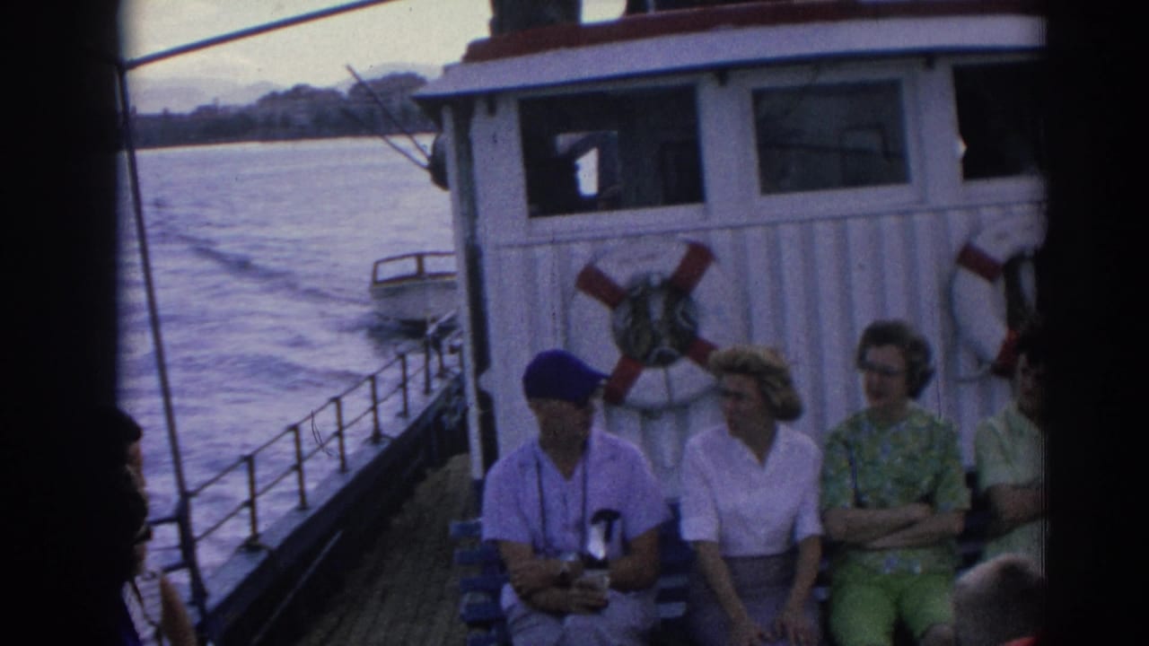 Izmir ferry passengers sit near the cabin and railing while the moving boat leaves a wake across the water.