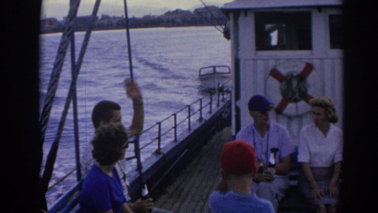 On the Izmir ferry deck, seated adults appear near life rings while another passenger raises an arm beside rigging and railings.