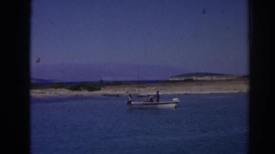 1962 8mm home-movie frame from near Izmir, Turkey, showing a small motorboat carrying several people across blue coastal water.