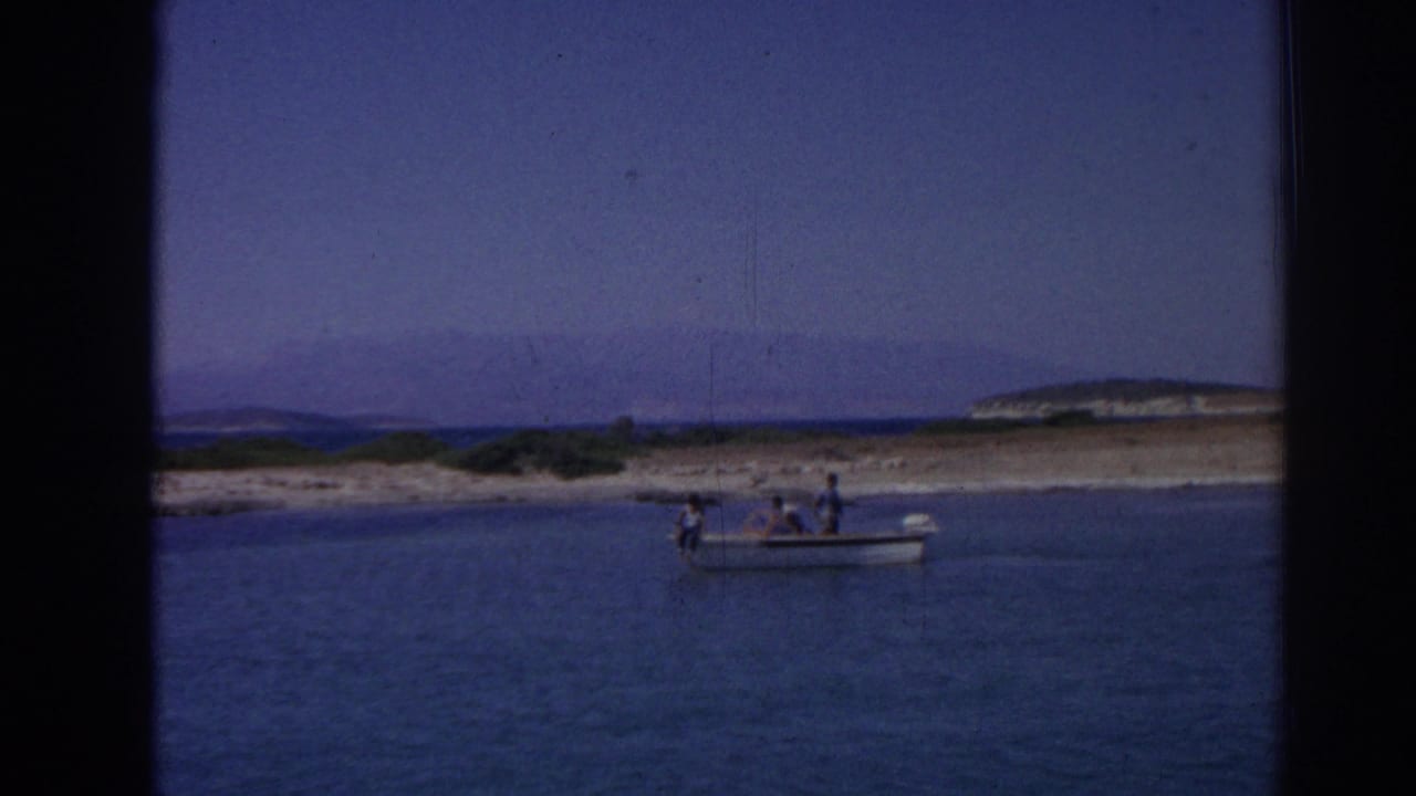 Small motorboat with distant passengers on blue water near Izmir, Turkey, with low coastal land and hills in the background.