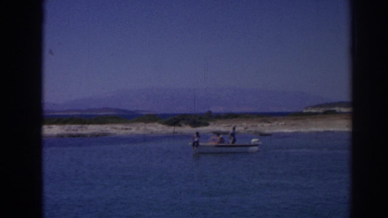Distant 1962 home-movie view of a small boat on coastal water near Izmir, with passengers visible and hills beyond the shore.