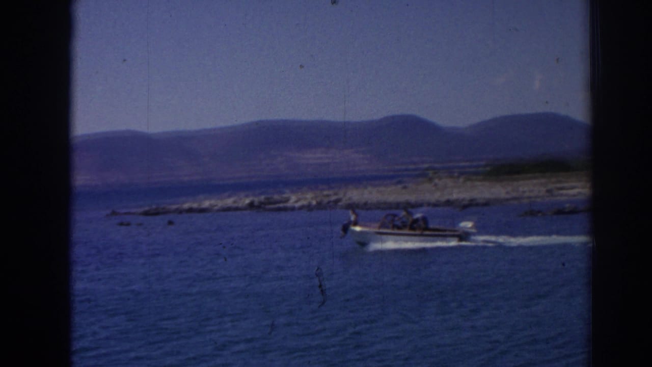 1962 Izmir-area coastal frame showing a small motorboat underway on rippled blue water, with passengers and distant hills visible.