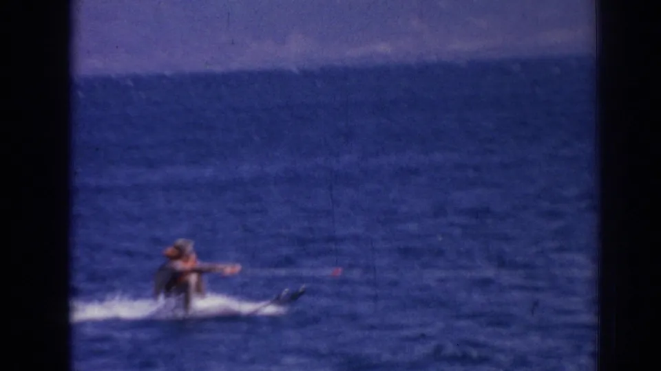 In 1962 Izmir home-movie footage, a distant water skier in an orange life jacket moves across choppy blue water.