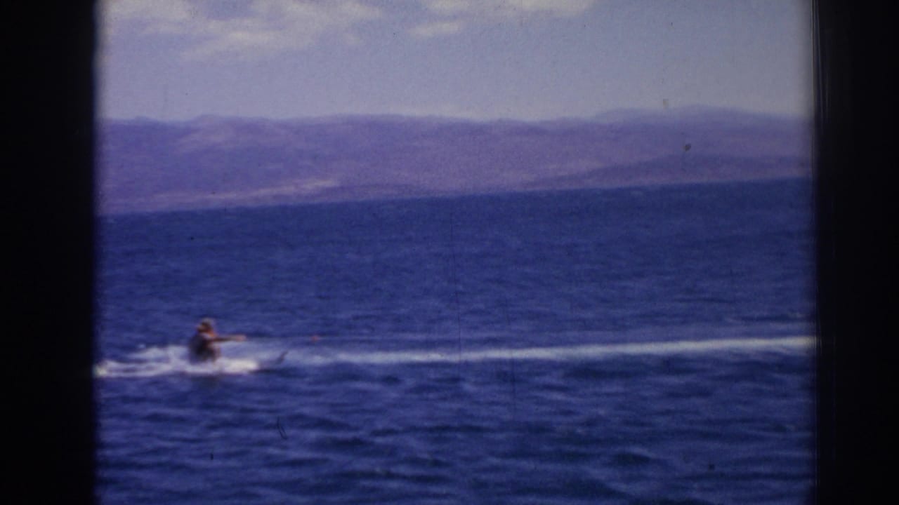 A distant skier is towed across the sea near Izmir, with white spray and mountains beyond the water.
