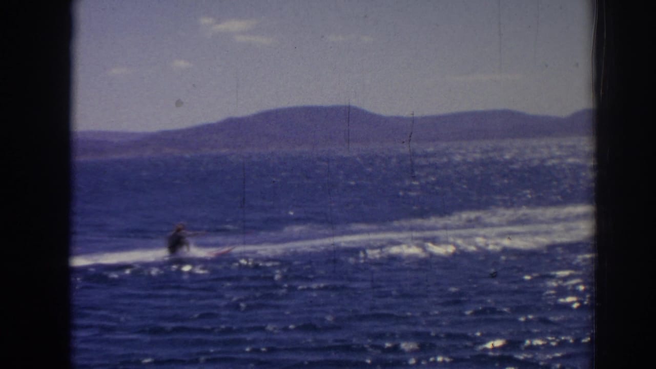 A distant water skier crosses sparkling blue water in 1962 Izmir footage, with hills visible along the far shore.