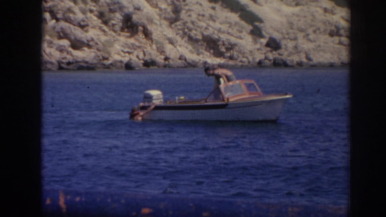 Small white motorboat on blue water with rocky coast behind it.