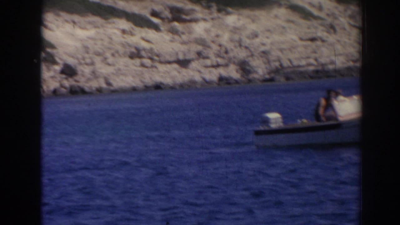 1962 Izmir frame with the motorboat partly cropped at right, passengers visible against blue water and a rocky coast.