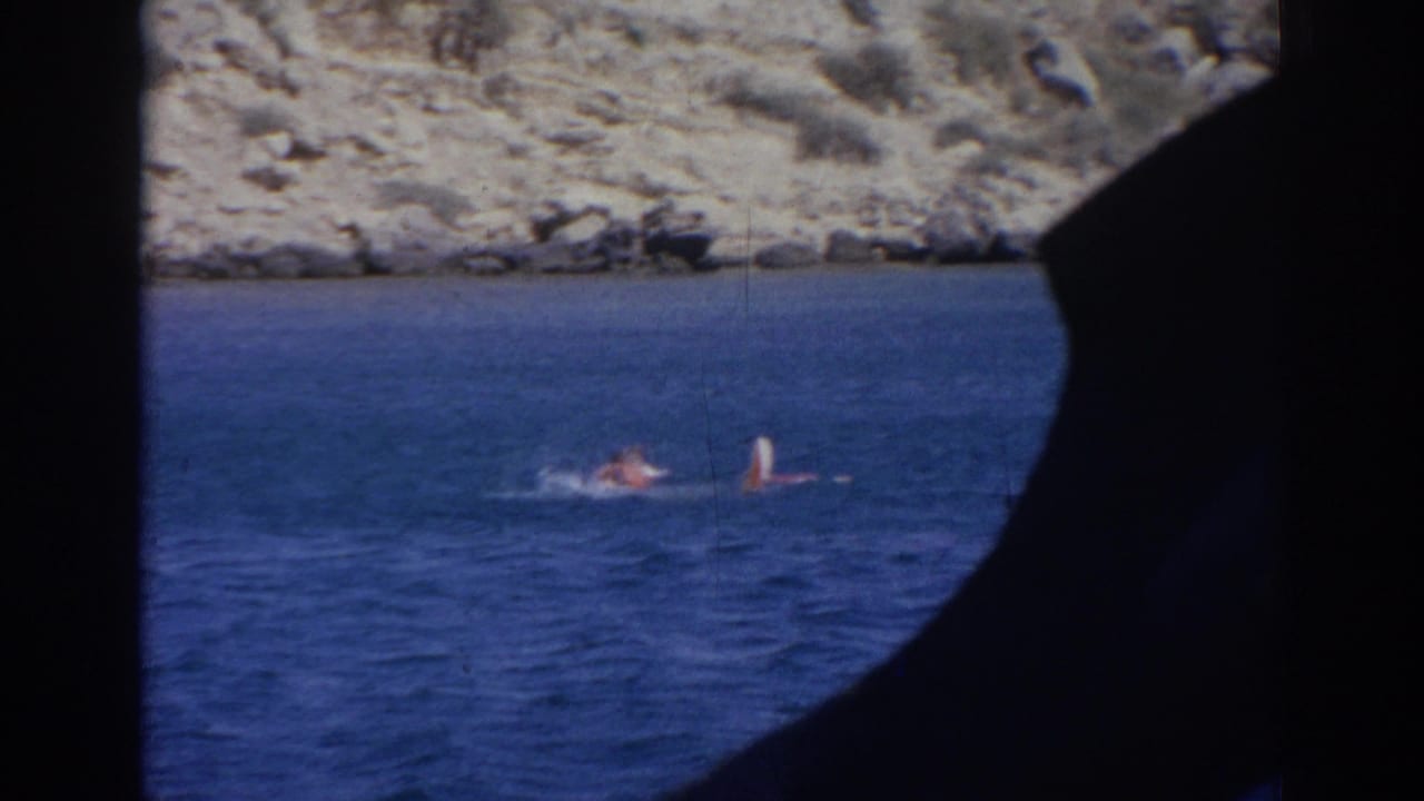 1962 Izmir frame showing swimmers splashing in coastal water, seen from behind a dark structural silhouette.