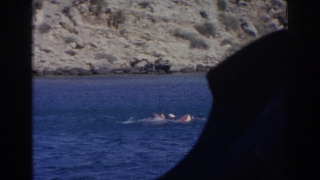 1962 Izmir coastal frame with partly submerged swimmers splashing near shore, obscured by a dark foreground silhouette.
