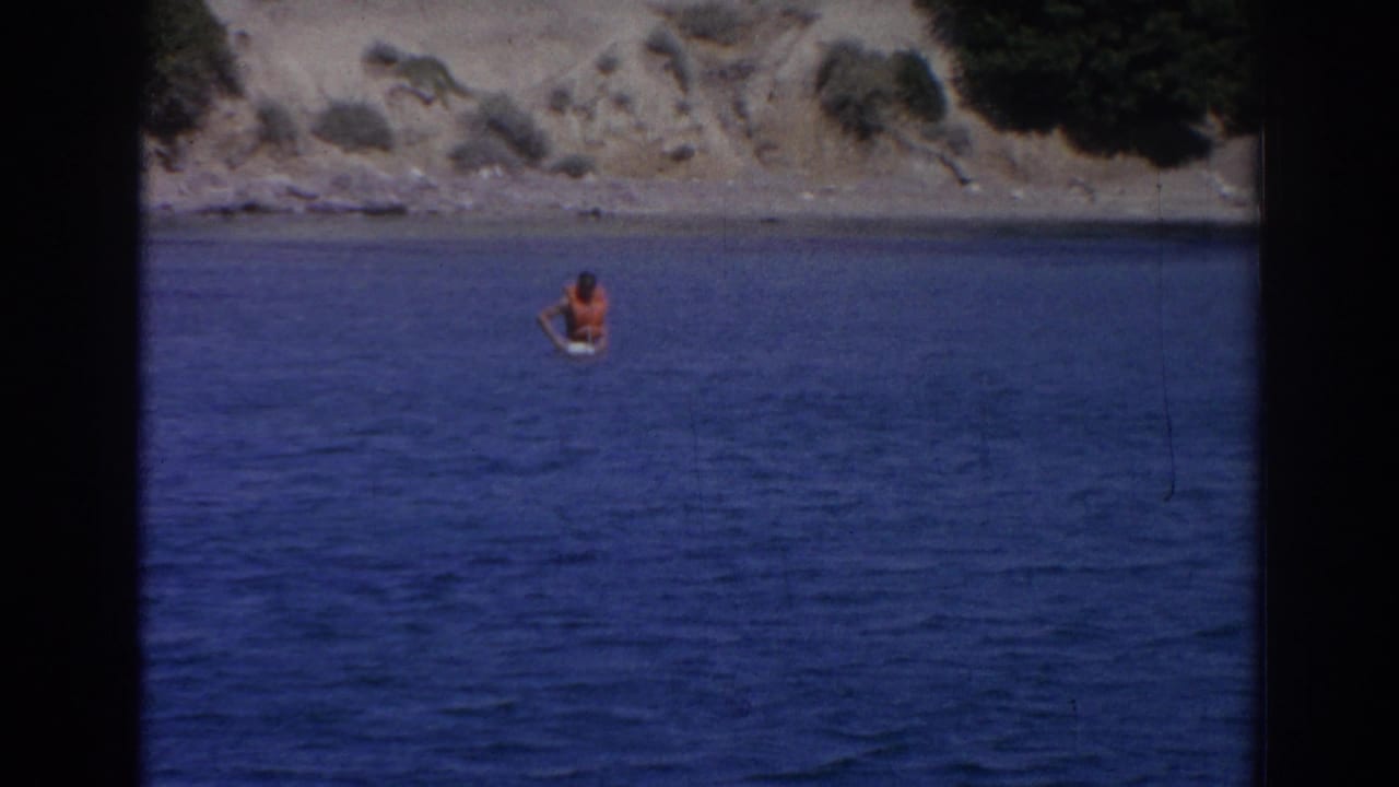 Distant swimmer in blue water near a rocky shoreline.