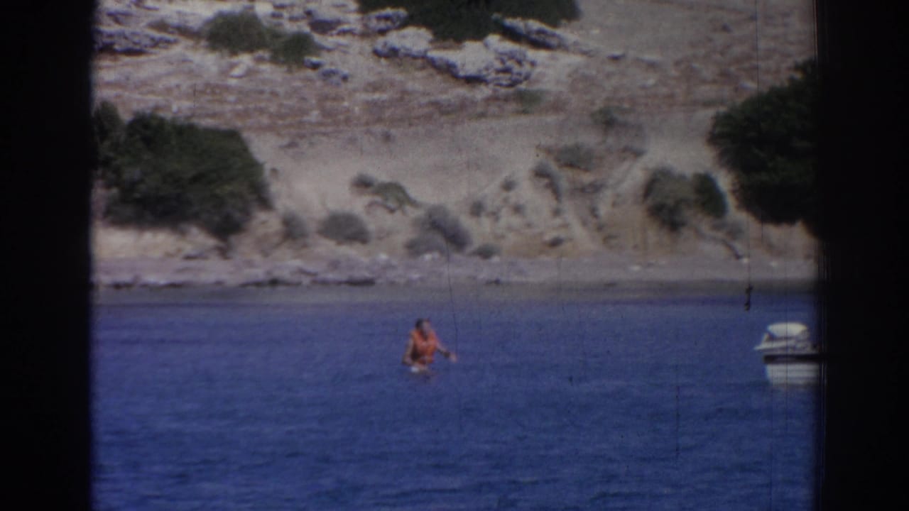 Person in an orange swimsuit wading or swimming near a rocky Izmir shoreline, with a small boat partly visible at frame edge.
