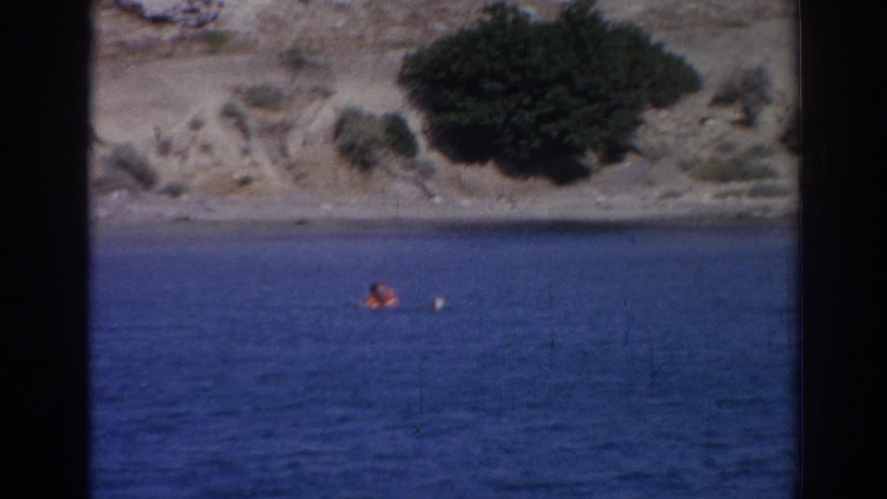 Distant 1962 Izmir coastal frame with a person in orange on the water and a small white float or board nearby.
