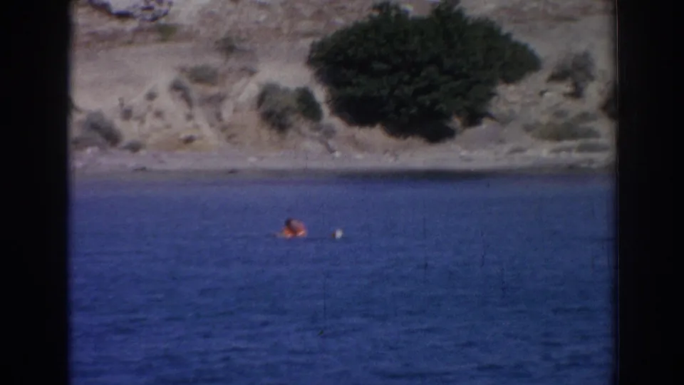 Distant 1962 Izmir coastal frame with a person in orange on the water and a small white float or board nearby.