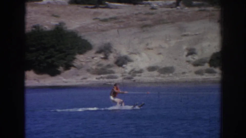 1962 Izmir home-movie frame showing the skier being pulled upright on water skis, leaving a small wake behind.