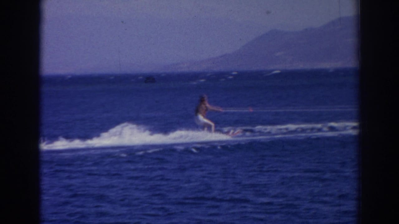 A water skier travels across the bright blue sea with distant mountains visible in 1962 Izmir home-movie footage.