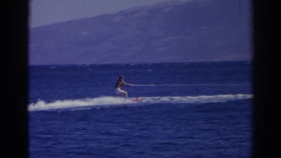 The skier remains low in frame, crossing choppy water beneath hazy mountains in the Izmir coastal scene.