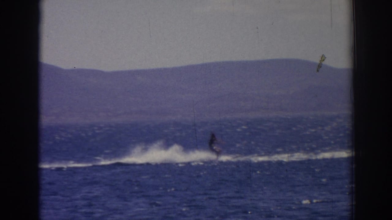 Distant water skier crossing a blue lake with white spray and mountains beyond.