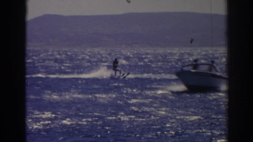 The towing motorboat becomes visible in this 1962 Turkey home-movie frame as the skier trails behind across the lake.