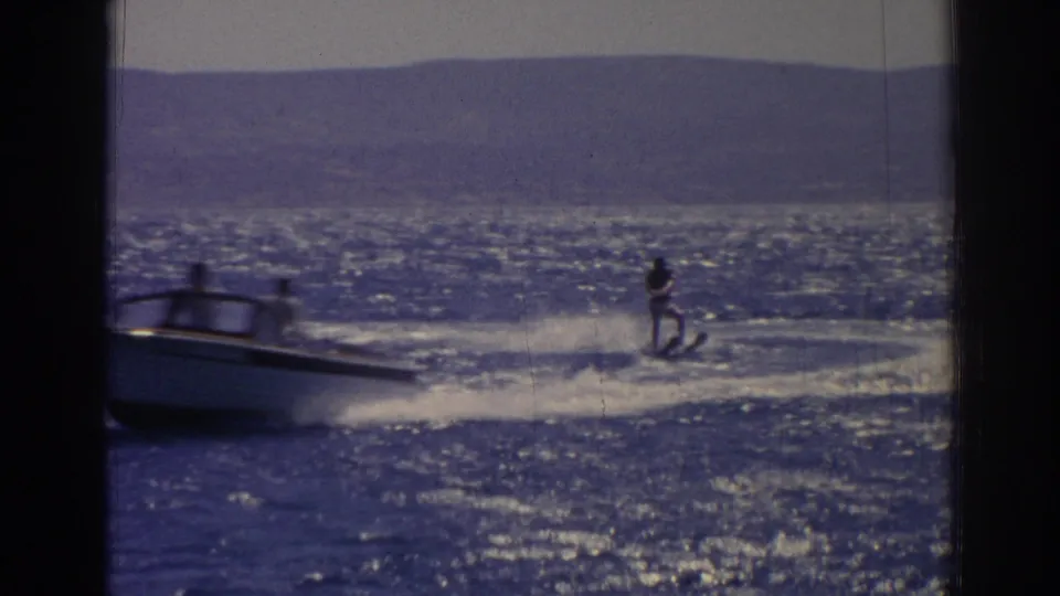 A small boat tows a distant water skier across the sparkling lake in the Izmir, Turkey, 1962 home-movie scene.