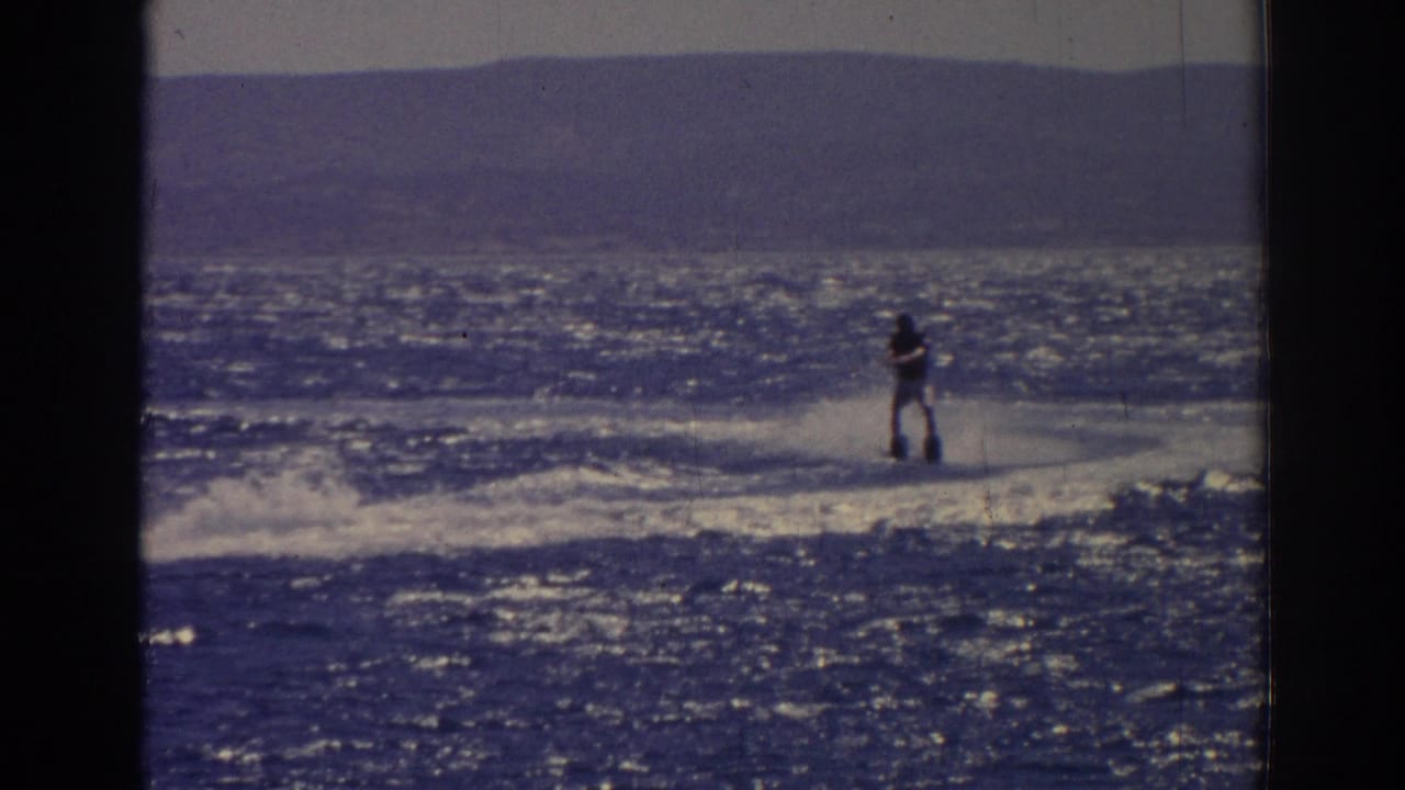 Distant water skier crosses sparkling water with hills in the background.