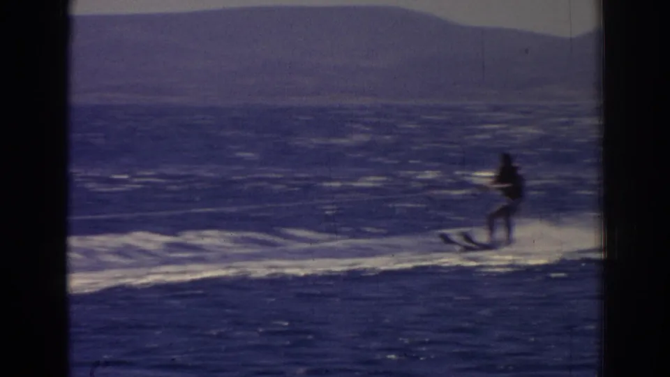 The skier appears slightly blurred while moving along a bright foamy wake, with hills faintly visible beyond the water.
