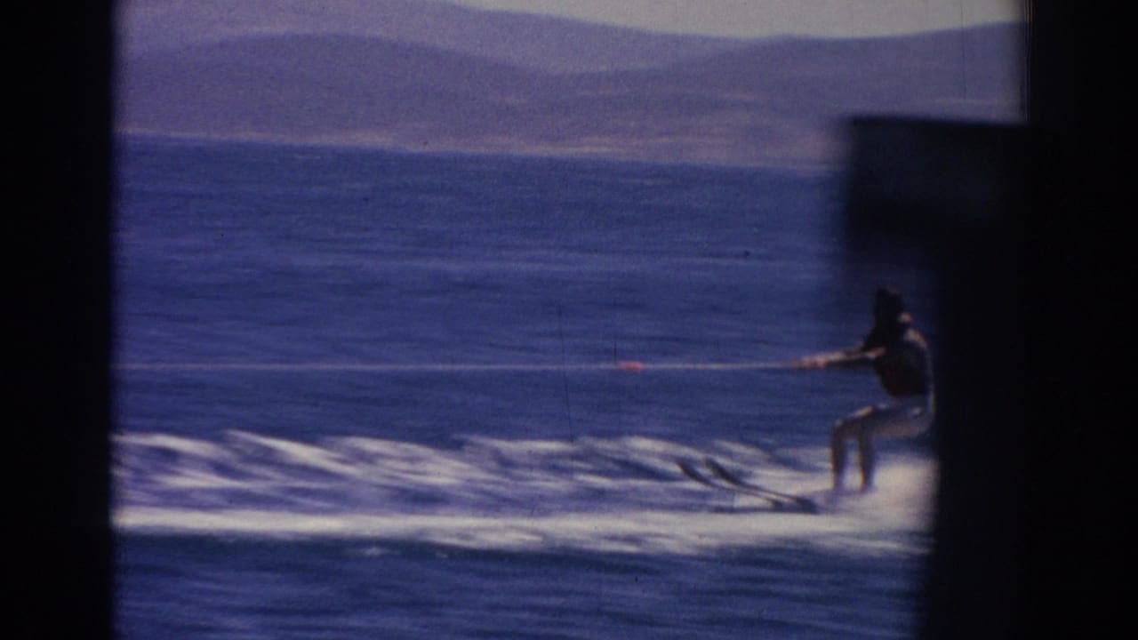 Distant waterskier crosses blue water beside a dark vertical window edge.