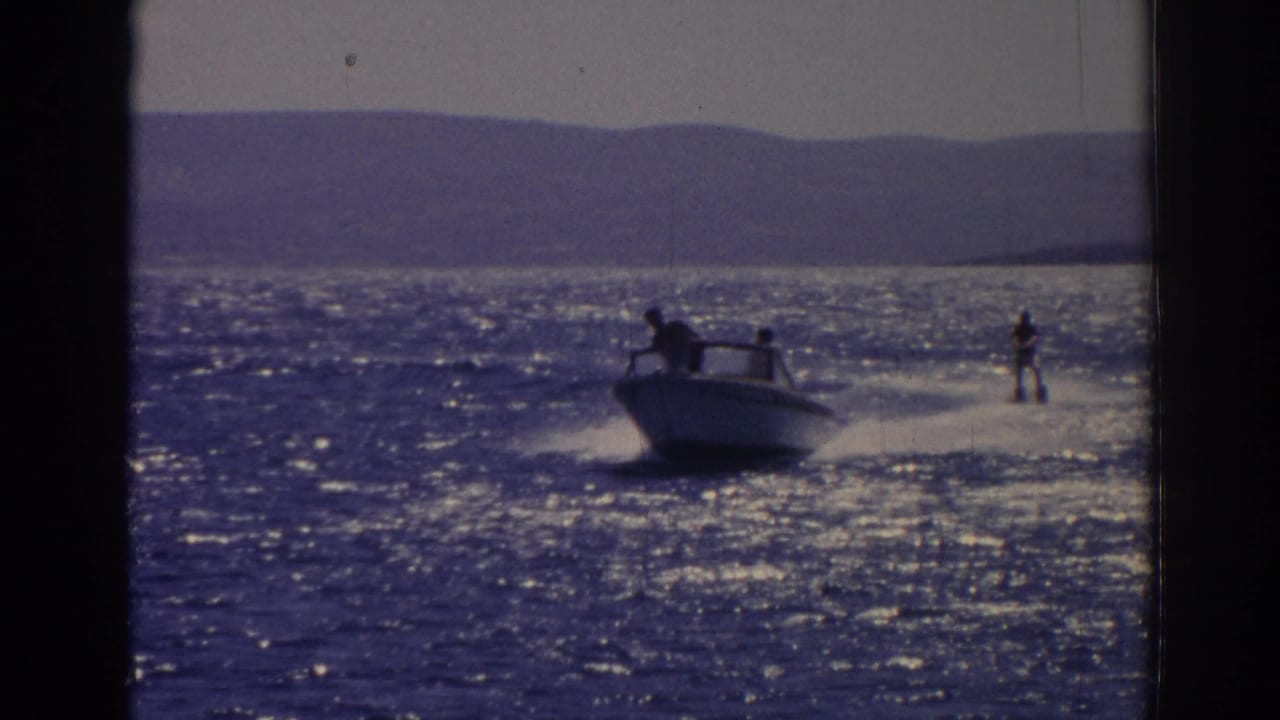 Motorboat pulling a water skier across bright open water with distant hills behind.