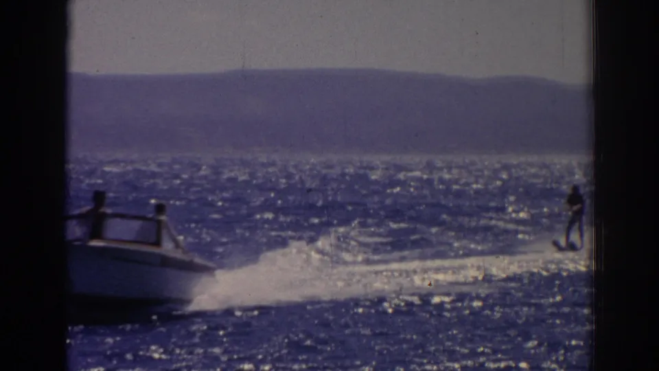 A cropped 1962 Izmir frame catches the boat exiting left while the water skier remains visible on the right side of the wake.