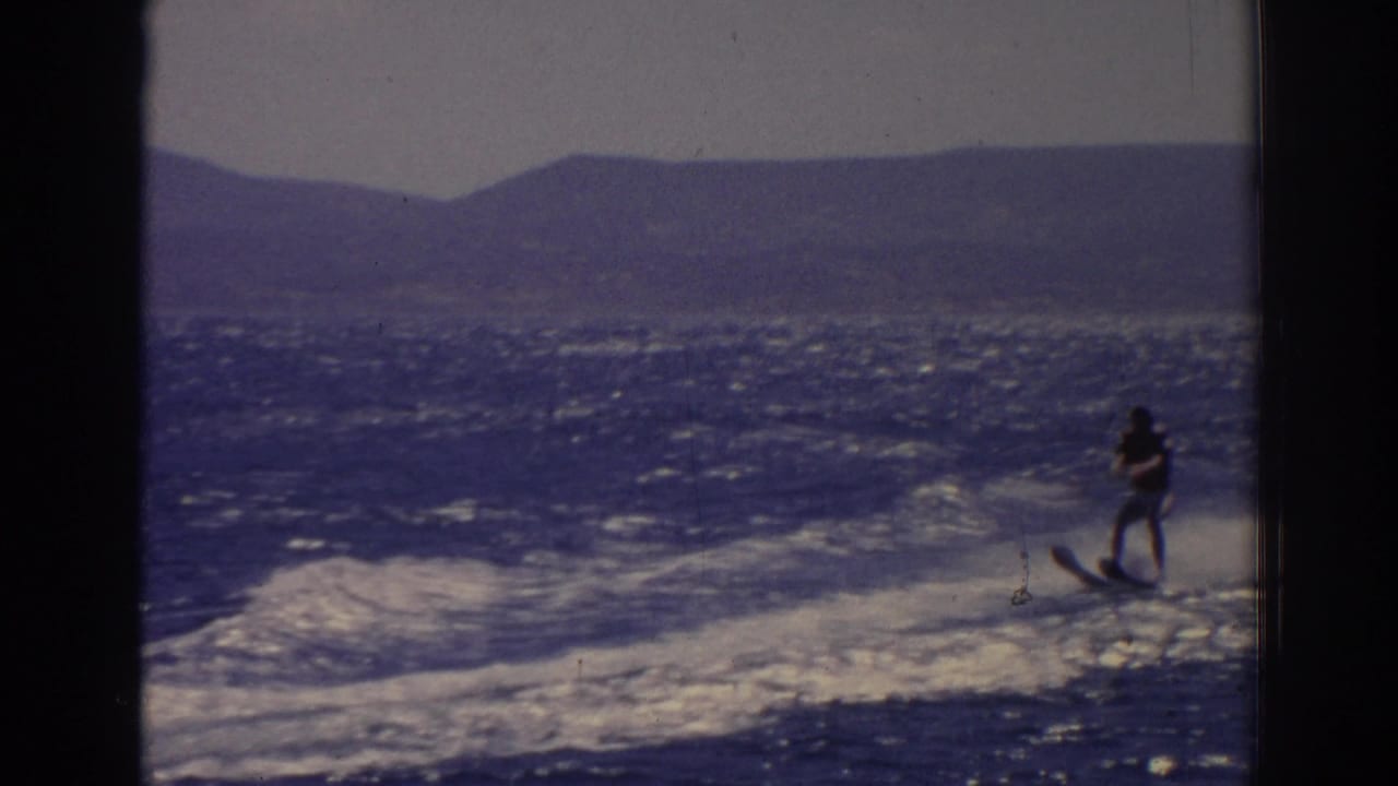 Man water skiing across choppy blue water with hills in the distance.