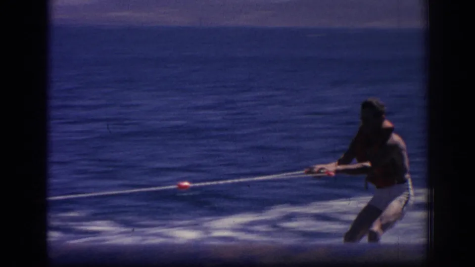 Near the end of the clip, the skier appears closer to the camera, holding the tow rope as the blue water fills most of the frame.