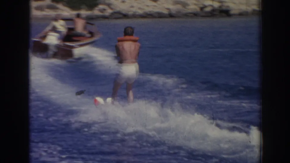 A small motorboat pulls the water skier through choppy wake, with rocky shoreline visible in the background of the Izmir footage.